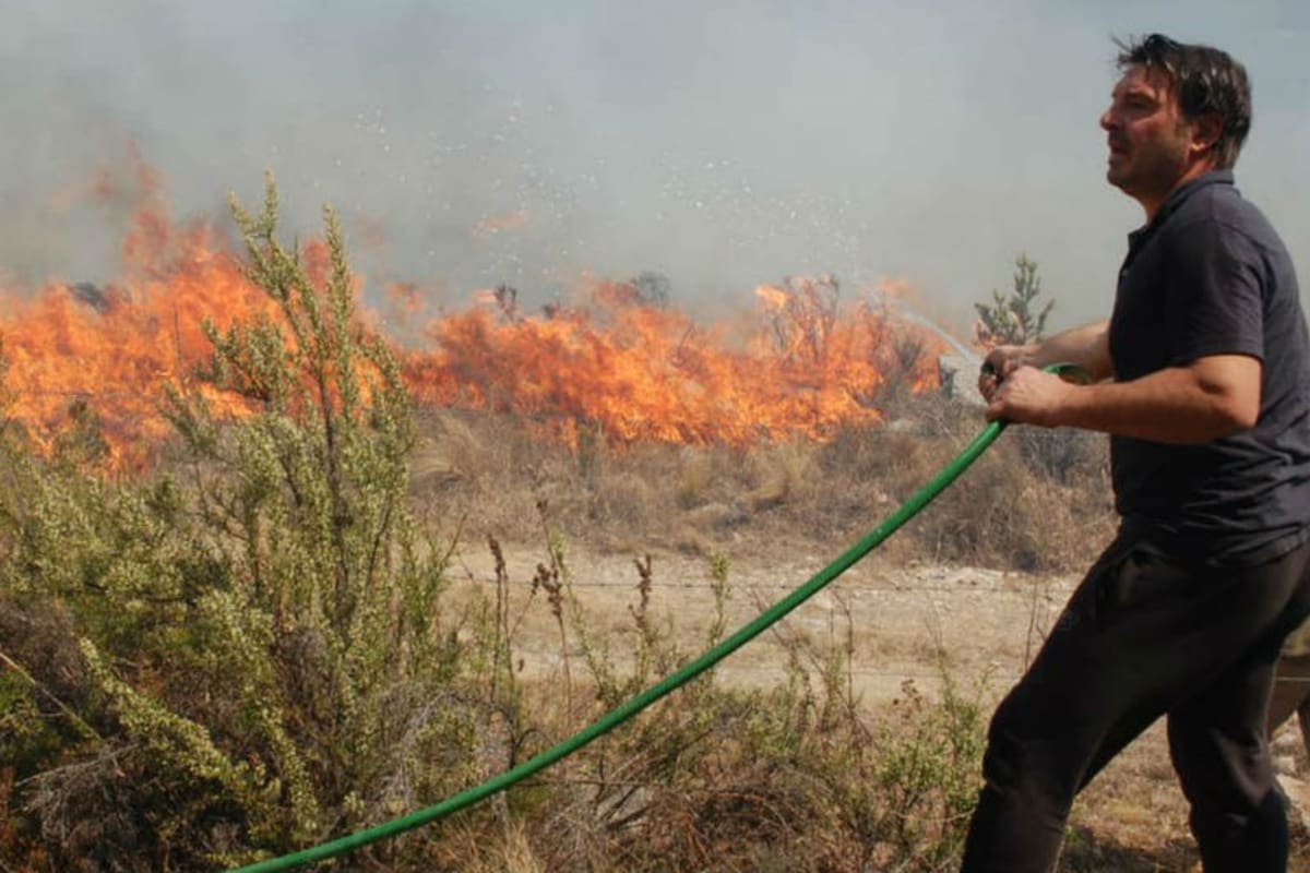 El actor, en la tarde del martes, intentando apagar el fuego para que no se acerque a su complejo de cabañas