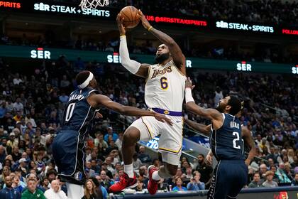El alero de los Lakers de Los Ángeles LeBron James lanza el balón frente a Justin Holiday y Kyrie Irving de los Mavericks de Dallas en el encuentro del domingo 26 de febrero del 2023. (AP Foto/LM Otero)
