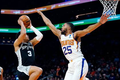 El alero de los Spurs de San Antonio Keldon Johnson intenta un disparo ante el alero Mikal Bridges, de los Suns de Phoenix, en la primera mitad del juego del lunes 5 de diciembre de 2021, en Phoenix. (AP Foto/Ross D. Franklin)