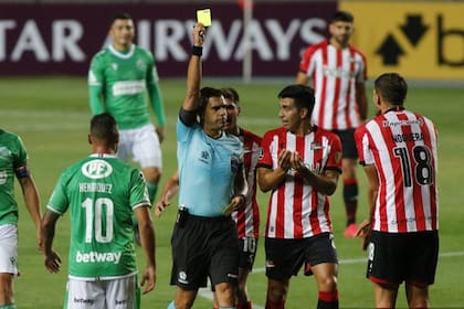 El arbitro Christian Ferreyra, de pobre labor, le muestra la tarjeta amarilla a Fabián Noguera