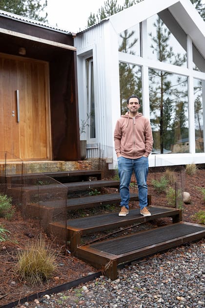 El arquitecto Tulio Rossini en el ingreso, con escalones de hierro. Los dobles vidrios polarizados matizan el reflejo de la nieve hacia el interior de la casa. Además, al tener exterior espejado, los ventanales muestran el bosque.