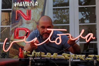El artista cubano Kadir López Nieves, que está restaurando los letreros de neón de la ciudad, posa con una lectura, "Victoria", en su taller y galería, en La Habana