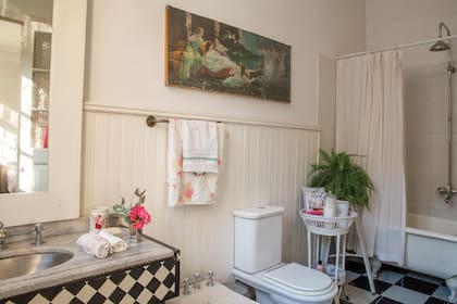 El baño, con piso de damero; motivo que se repite en vanitory. También hay flores, canastos patinados y cuadros.