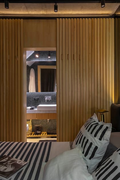 El baño en suite es negro con detalles en madera natural y luces indirectas cálidas y frías.