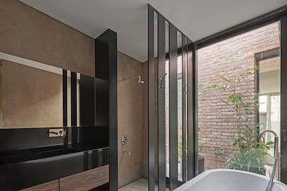 El baño tiene revestimiento en estuco color visón (Tarquini) y mueble de petiribí con mesada en mármol negro Brasil. A modo de mampara, un panel con tiras de hierro laqueado.