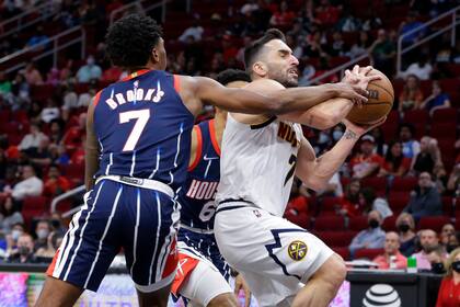 El base argentino Facundo Campazzo, derecha, de los Nuggets de Denver, recibe una falta de Armoni Brooks, de los Rockets de Houston, en duelo de NBA el sábado 1 de enero de 2022, en Houston. (AP Foto/Michael Wyke)