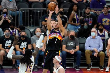 El base de los Suns de Phoenix Devin Booker lanza el balón superando a Montrezl Harrell y Alex Caruso de los Lakers de Los Ángeles en el encuentro de la primera ronda de la postemporada del domingo 23 de mayo del 2021. (AP Photo/Ross D. Franklin)