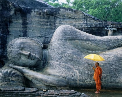 Un monje al lado de una escultura de un Buda acostado