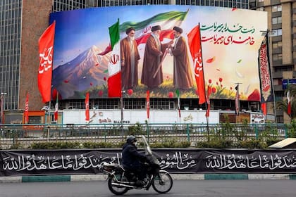 El cartel muestra al fallecido líder supremo de Irán Ruhollah Jomeini, observando cómo su sucesor, el difunto ayatollah Alí Khamenei, entrega la bandera nacional a su hijo y nuevo líder supremo, Mojtaba Khamenei.
