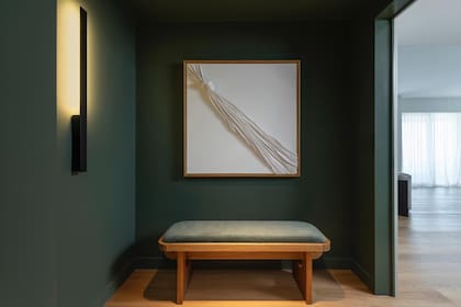 El cuadro, hecho a medida y pensado exclusivamente para ese espacio, por Gabriela Herman. Banco (Taller Ferro) y aplique de pared (Dimm). El color en la pared, Rosemary (SW6187, Sherwin Williams).