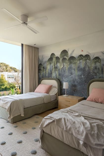 El cuarto de las hijas, revestido con el mural ‘Bosque de los Magos’ (Mercedes Costal), tiene camas con respaldo entelado (Melazza) y alfombra ‘Pompones’ (Elementos Argentinos).