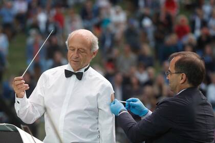 El director Ivan Fischer, fundador de la Orquesta del Festival de Budapest, recibe su tercera dosis de la vacuna contra el COVID-19 mientras dirige a la orquesta en un concierto gratuito al aire libre en Budapest, Hungría, el miércoles 25 de agosto de 2021. (AP Foto/Laszlo Balogh)