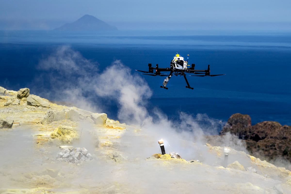 El dron pilotado por vulcanólogos de la Universidad de Múnich sobrevuela la zona durante una misión para recopilar datos sobre las emisiones de gases en el cráter de La Fossa, en la isla de Vulcano, una de las siete islas del archipiélago de las Eolias, en Sicilia, el 9 de julio de 2026. Un equipo de investigadores alemanes está probando un nuevo sistema para medir los gases volcánicos y así predecir mejor futuras erupciones. Sobrevolando el cráter de La Fossa, el dron se posiciona frente a un rayo láser situado en el borde del abismo en Vulcano, frente a la costa de Sicilia, para recopilar datos. (Foto de Marco Bertorello / AFP)