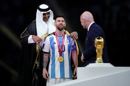 El Emir de Qatar, Sheikh Tamim bin Hamad Al Thani, parece colocarle a Messi la capa de superhéroe; observa Gianni Infantino, presidente de la FIFA
