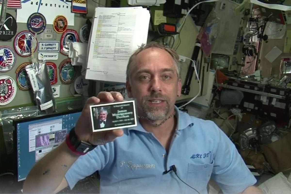 El empresario estadounidense Richard Garriot, uno de los turistas que viajaron al espacio en 2008, junto a la tarjeta plastificada con las cenizas de James Montgomery Scott desde la Estación Espacial Internacional