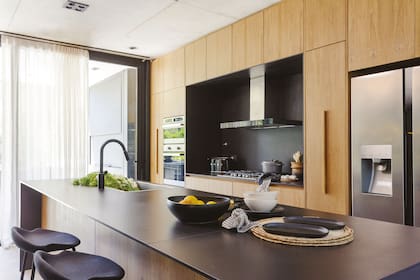 El equipamiento de la cocina (De Otro Tiempo) fue realizado con enchapado de petiribí natural. Banquetas de aluminio negras ‘Eros’ (Andy Forn Casa).