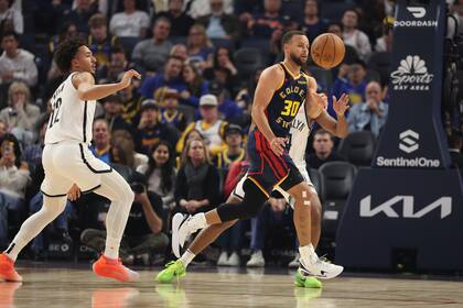 El escolta de los Warriors de Golden State, Stephen Curry (30), pasa el balón contra el alero de los Nets de Brooklyn, Jalen Wilson, a la izquierda, durante la primera mitad de un partido de baloncesto de la NBA en San Francisco, el lunes 25 de noviembre de 2024. (AP Foto/Jed Jacobsohn)