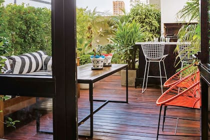 El espacio al aire libre se trazó como un auténtico ambiente, y se organizó en dos zonas: junto a la parrilla, la barra con banquetas ‘Bertoia’; cerca de la puerta, un living con sillas ‘Acapulco’, mesa baja y sillón de madera con almohadones impermeables.