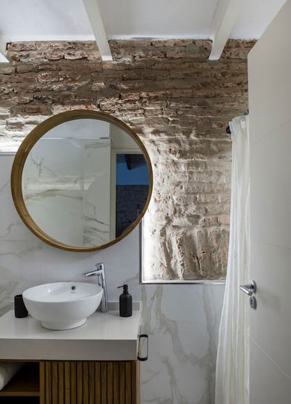 El espejo circular con marco de madera, mesada y mueble varillado se repiten en el toilette.