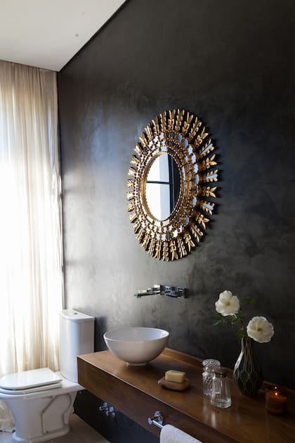 El espejo redondo con marco metalizado se destaca sobre la pared en gris azulado y le da un aire sofisticado al baño en una obra del estudio Detry Miguens.