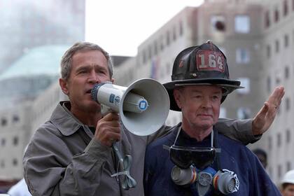 El expresidente estadounidense George W. Bush (izq.) habla junto al bombero retirado Bob Beckwith, de 69 años, con voluntarios y bomberos mientras examina los daños en el lugar del World Trade Center el 14 de septiembre de 2001 en Nueva York