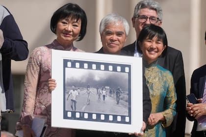 El fotógrafo Nick Ut, en el centro, junto a la protagonista de su foto ganadora del premio Pulitzer, Phan Thi Kim Phuc, a la izquierda, sostiene "La chica del napalm" mientras esperan reunirse con el Papa Francisco en la Plaza de San Pedro, en el Vaticano, en 2022