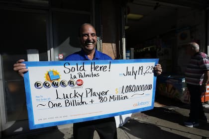 El funcionario de la lotería, Rick Herrera, sostiene un cheque ampliado en el exterior de Las Palmitas Mini Market, donde se vendió el boleto ganador de la lotería Powerball, en el centro de Los Ángeles, el jueves 20 de julio de 2023