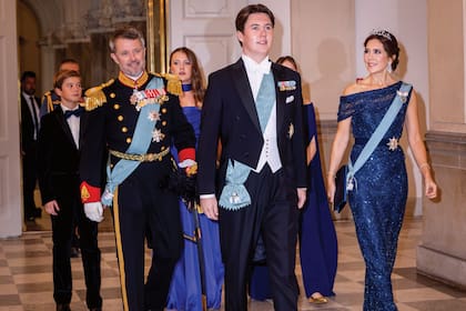 El homenajeado entró a la recepción a paso firme, vestido con un jaquette oscuro, camisa y moño blancos y zapatos negros, y lució una banda azul sobre su pecho y distinciones en la solapa. Detrás de él, su padre, el príncipe real Federico, con uniforme de gala. Su madre, Mary, con un diseño de lentejuelas de escote asimétrico del diseñador Jesper Høvring; clutch satinado de Prada y sandalias de Gianvito Rossi. La princesa llevó, además, la tiara que sus suegros le regalaron para su boda, una pieza de oro blanco, diamantes y perlas.