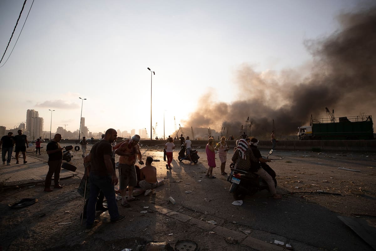 El humo se ve al fondo mientras algunas personas evacuan la zona cercana al accidente con explosivos, en Beirut
