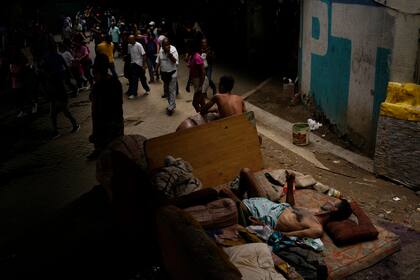 El indigente César Ramírez yace en un colchón debajo de un puente mientras los trabajadores públicos marchan en protesta en Caracas, Venezuela, el jueves 11 de agosto de 2022.  (AP Foto/Matías Delacroix)