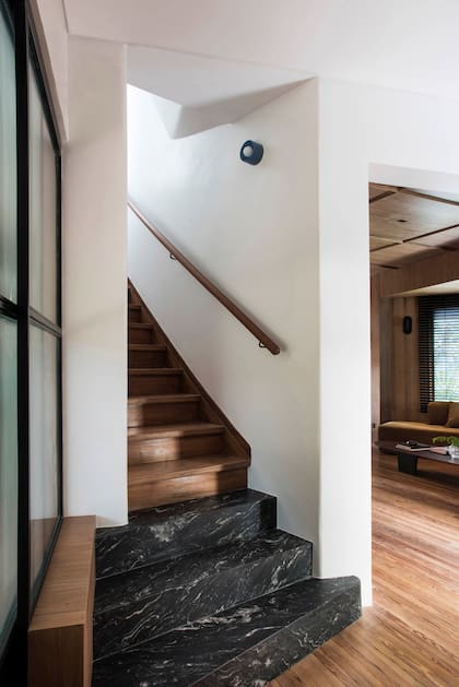 El inicio de la escalera está junto a la puerta de vidrio que lleva a la cocina y queda oculta del living, en el ambiente contiguo. Escalones revestidos en granito ‘Amadeus’ (De Stefano por Aranda Mármoles). Aplique de pared (Dynamo).