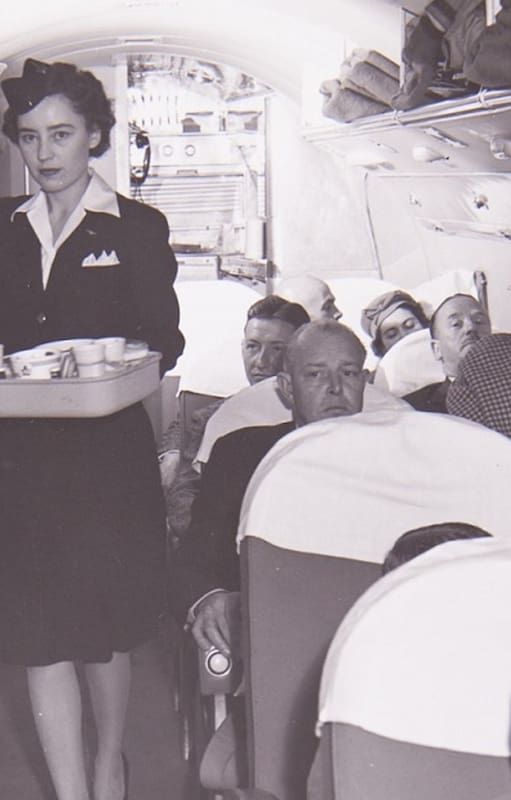 El interior de un Douglas DC-3 y una azafata, en los años previos a la división de los aviones en clases