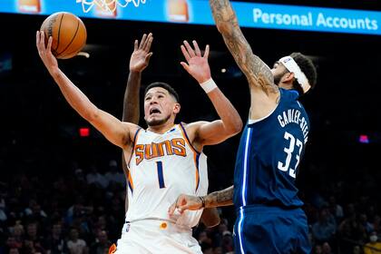 El jugador de los Suns de Phoenix Devin Booker (1) tira a canasta frente al jugador de los Mavericks de Dallas Willie Cauley-Stein (33) en la segunda mitad de su juego de NBA el miércoles 17 de noviembre de 2021 en Phoenix. (AP Foto/Matt York)
