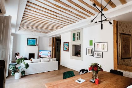 El living comedor con vigas a lo largo del techo y una ventana en una de las paredes laterales conduce a la cocina. A un costado se destacan pequeños cuadros y retratos, entre ellos, un setlist escrito por Kurt Cobain de un concierto de Nirvana.