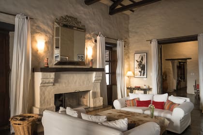 El living de la casa está cálidamente decorado con muebles de madera rústica, sofás blancos, mantas de tejidos locales y alfombras de colores fuertes.