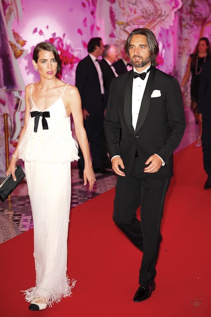 El look de Charlotte Casiraghi (en la foto con su marido, Dimitri Rassam), representó como ningún otro el espíritu feliz de la década del 20. De la colección Alta Costura Primavera-Verano 2022 de Chanel, se trata de un conjunto blanco con adornos de pedrería y top con breteles, con un lazo negro en el pecho y terminado en plumas y flecos, detalle con el que también termina la larga falda. Completó su outfit con clutch negro, zapatos bicolor y un falso bob recogido con un adorno plateado y peinado con ondas en los mechones, al más puro estilo años 20.