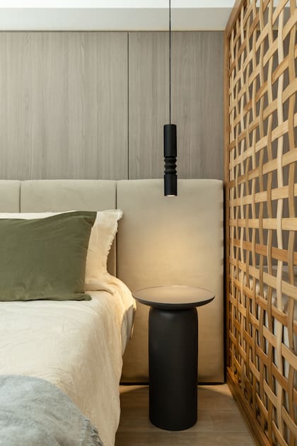 El mismo lenguaje: tanto la mesa de luz como la luminaria son torneadas. El divisor de madera actúa como separador, pero es permeable al paso de la luz.