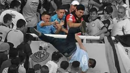 El momento en el que Balbo cae de la tribuna; lo empujan Martín Vergara (de rojo), Cristian Oliva (de gorra blanca), Pablo Robledo (el segundo de la izquiera) y Matías Oliva (el primero de la izquierda)