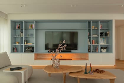 El mueble (Arq & Co) que atraviesa todo el sector social cumple con el pedido de sumar espacio de guardado; además, varía sus funciones según el sector: frente al sillón, aloja el televisor, un biohogar y biblioteca.