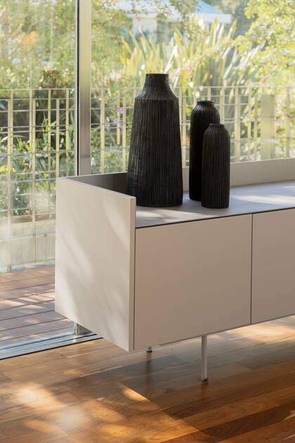 El mueble de la TV también es bar, hecho de madera laqueada con lustre semimate (Sherwin-Williams) y estructura metálica en el mismo tono. Jarrones (Andy Forn Casa).