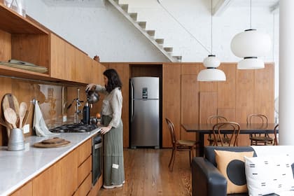 El mueble recorre todo el ambiente y alterna las funciones. Además de cocina y despensa, oculta el toilette y lavadero, que se encuentran detrás.