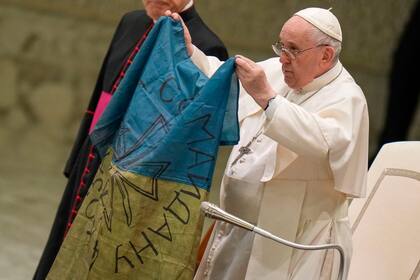 El papa Francisco alza una bandera ucraniana que le llevaron desde Bucha, Ucrania, durante su audiencia general semanal en la sala Pablo VI, Ciudad del Vaticano, miércoles 6 de abril de 2022. (AP Foto/Alessandra Tarantino)