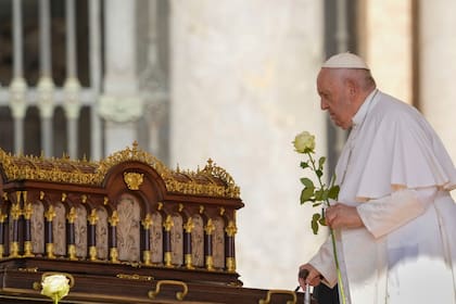 El papa Francisco, con una rosa en la mano, se dispone a rezar ante las reliquias de Santa Teresa del Niño Jesús, patrona universal de las misiones (izquierda), a su llegada a la audiencia nacional en la Plaza de San Pedro, en el Vaticano, el 7 de junio de 2023. (AP Foto/Andrew Medichini)