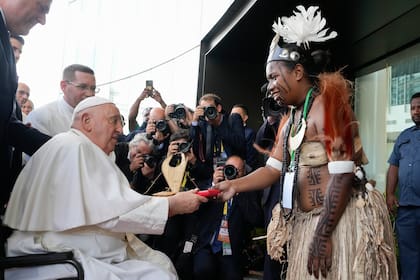 El papa Francisco entrega un regalo a un intérprete de bailes tradicionales a su llegada a APEC Haus, en Puerto Moresby, Papúa Nueva Guinea, el 7 de septiembre de 2024. (AP Foto/Mark Baker)