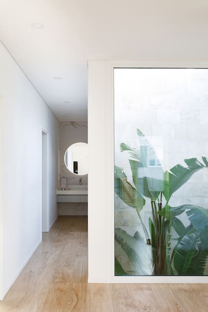 El pasillo desemboca en un antebaño abierto. El patio, con sus plantas, enmarca la pared de Travertino que contiene el baño.
