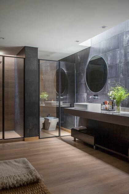 El piso ‘Fusion Vinilum’ (Patagonia Flooring) es el mismo en toda la suite. Revestimiento de pared de porcelanato (Ilva). Mesada de Silestone, bacha de apoyo y grifería (FV). Cerraron los sectores de baño y ducha con mamparas de vidrio con marco negro (Ideal Mamparas).