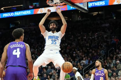 El pívot del Magic de Orlando Goga Bitadze (35) encesta mientras el pívot de los Suns de Phoenix Oso Ighodaro (4) y el escolta Tyus Jones (21) observan durante la primera mitad de un partido el lunes 18 de noviembre de 2024 en Phoenix. (AP Foto/Ross D. Franklin)
