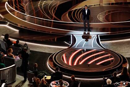El presentador Chris Rock habla en el escenario mientras Will Smith y Jada Pinkett, abajo a la izquierda, escuchan desde sus asientos durante la ceremonia de los premios Oscar, el domingo 27 de marzo de 2022 en el Teatro Dolby en Los Ángeles. (Foto AP/Chris Pizzello)