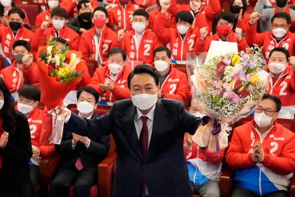 El presidente electo de Corea del Sur, Yoon Suk Yeol, sostiene ramos de flores mientras es felicitado por legisladores y miembros de su partido en la Asamblea Nacional, el 10 de marzo de 2022, en Seúl, Corea del Sur. (AP Foto/Lee Jin-man, Pool, Archivo)