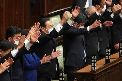 El primer ministro de Japón, Fumio Kishida (centro), y otros legisladores dan tres vivas tras disolver la cámara baja, la más poderosa de las dos del parlamento, durante una sesión extraordinaria, en Tokio, el 14 de octubre de 2021. (AP Foto/Eugene Hoshiko)